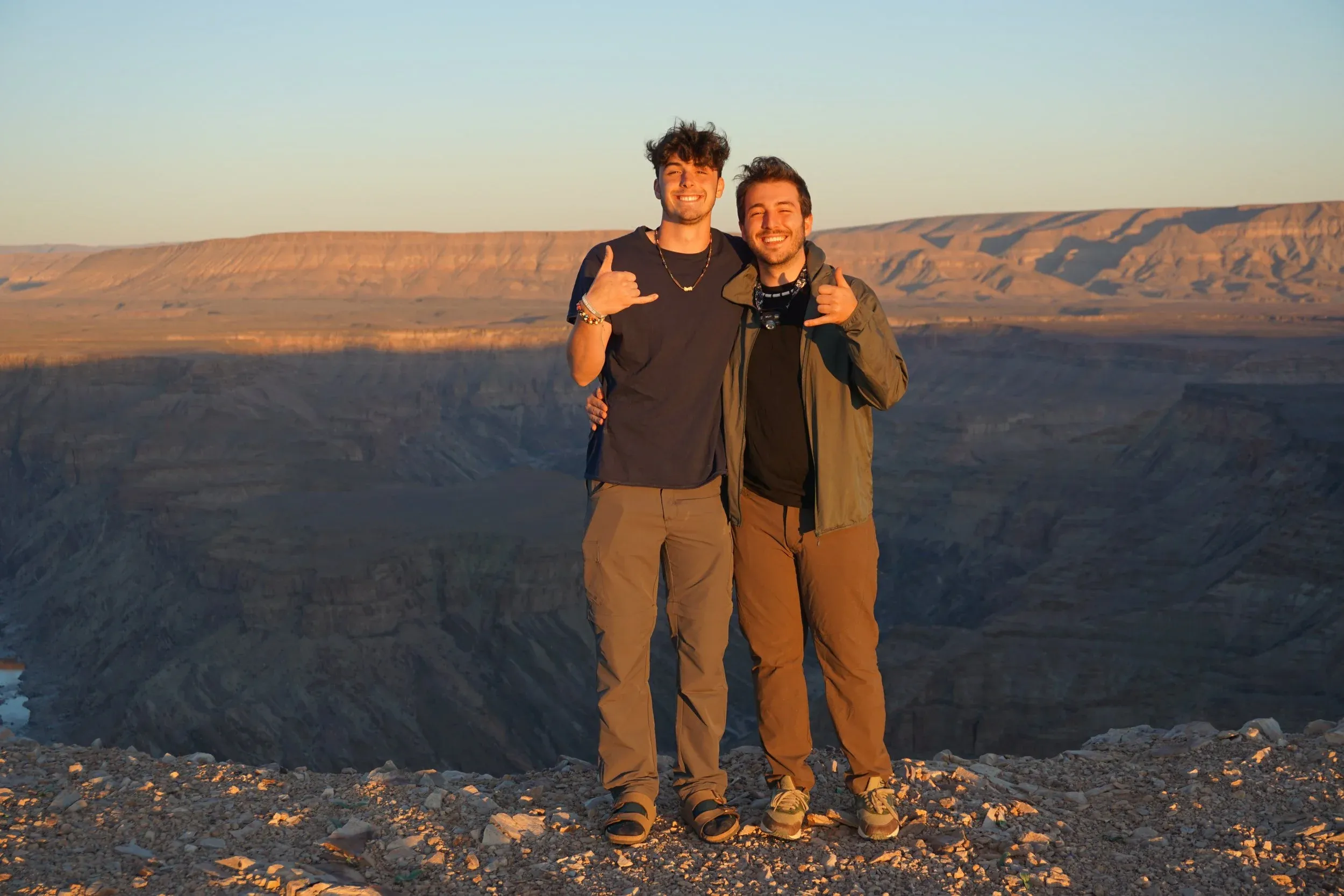 Two people posing on a cliff edge above a canyon at sunset