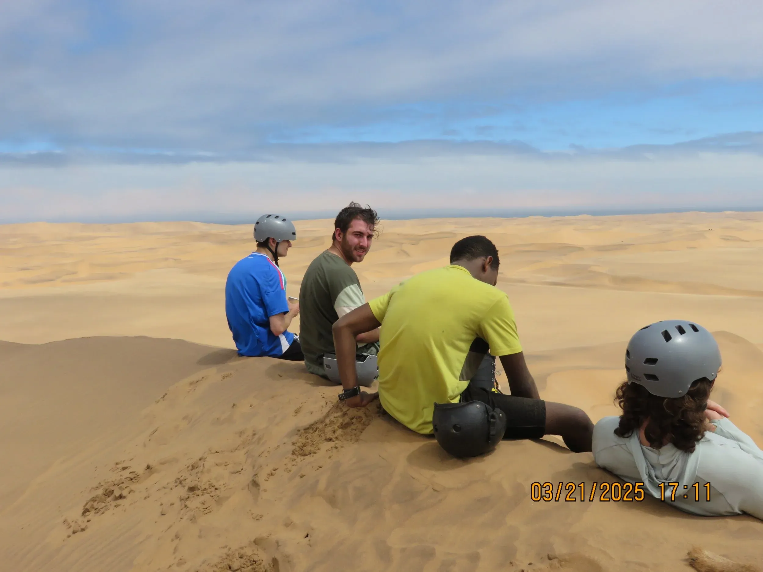 Three friends resting on top of a sand dune after sandboarding