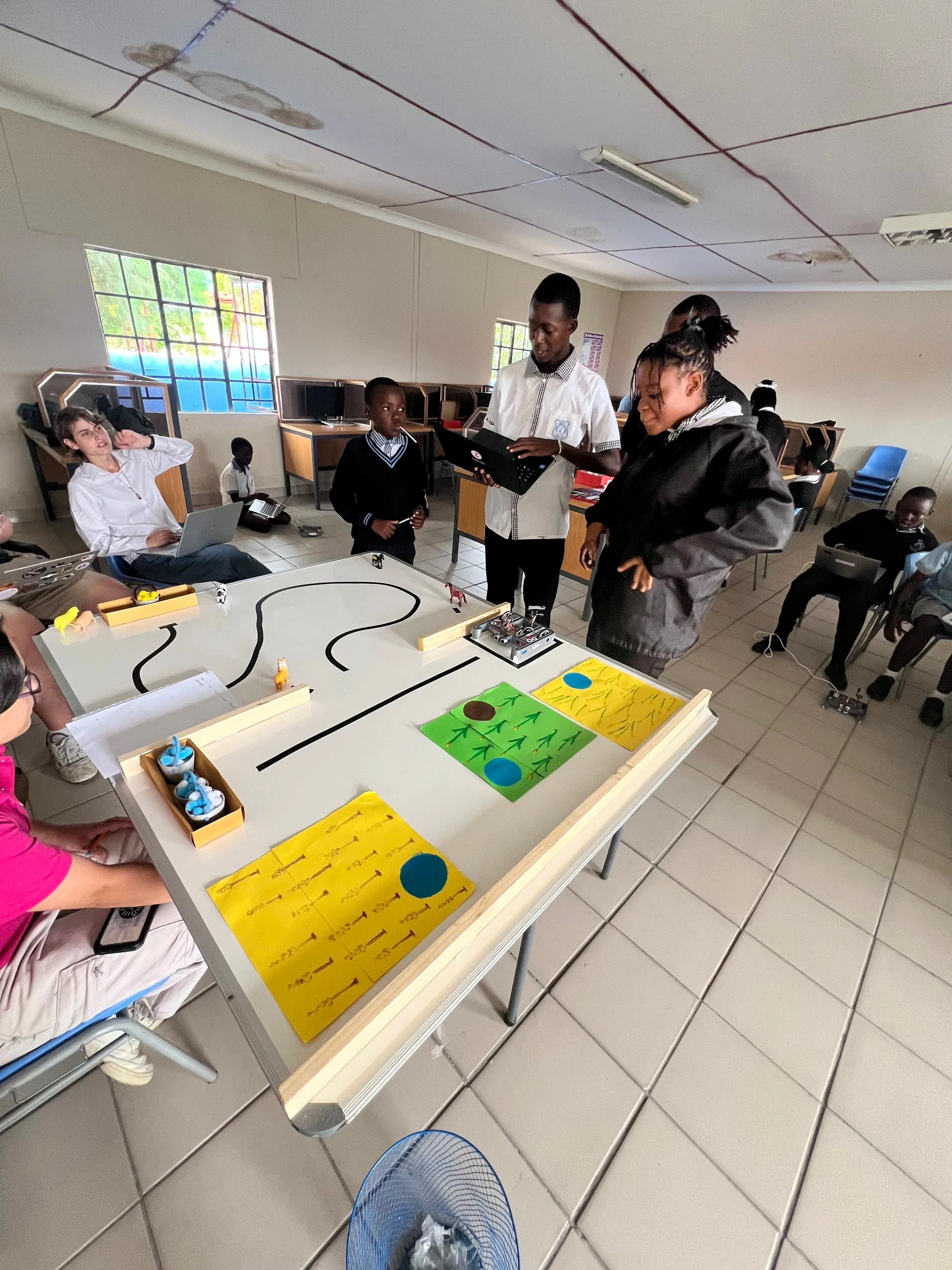 Students watching a small robot drive along a taped track during a lesson